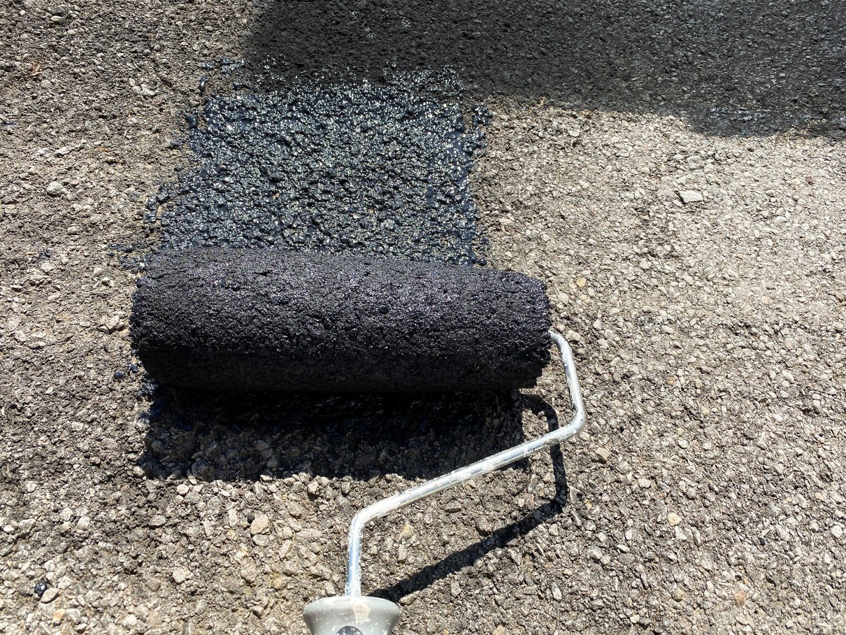 Roller being used to put black sealant paint on a tarmac driveway